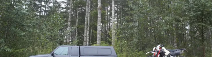 Un pick-up et une moto tout-terrain garés à l'orée d'une forêt dense de conifères.