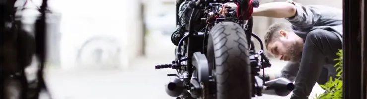 Un mécanicien barbu travaille minutieusement sur l'avant d'une moto en réparation dans un garage.