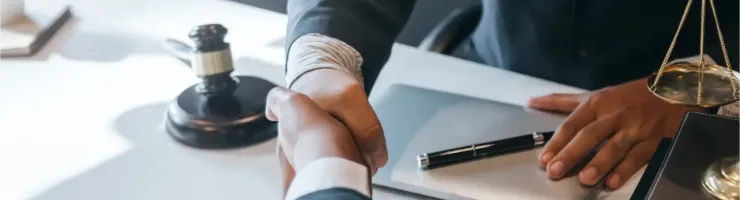 Deux hommes en costumes d'affaires se serrent la main au-dessus d'un bureau avec une balance de justice.