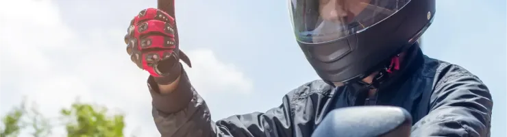 Un motard casqué avec des gants rouges lève le pouce, signifiant que tout va bien.