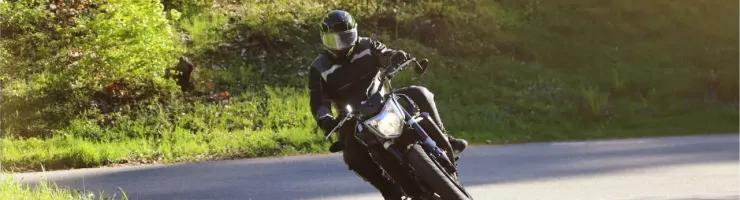 Un motard casqué se penche dans un virage sur une route sinueuse bordée d'arbres verdoyants.
