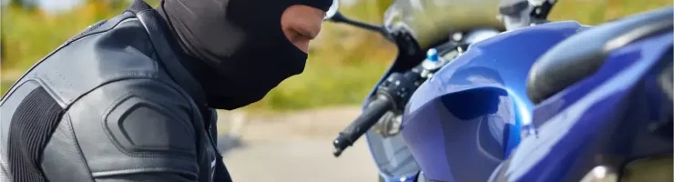 Un motard portant une cagoule noire et un blouson en cuir, près d'une moto bleue.