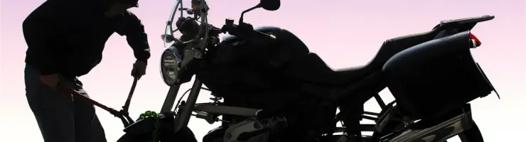 Silhouette d'un individu s'apprêtant à voler une moto à l'aide d'une pince coupante.