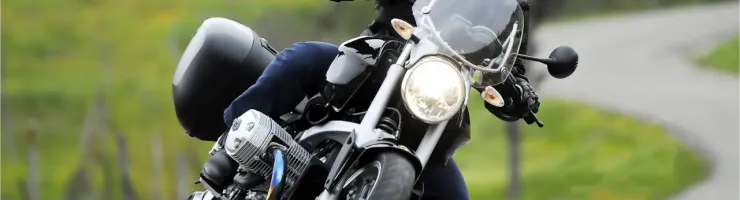 Un motard en tenue de cuir noir et casque s'incline dans un virage sur une route de campagne sinueuse et verdoyante.