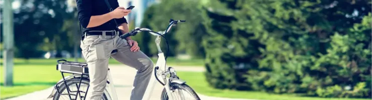 Un homme casqué et lunettes de soleil, assis sur un vélo électrique blanc, regarde son téléphone.