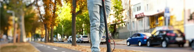 Un homme roule sur une trottinette électrique sur une piste cyclable bordée d'arbres en automne.