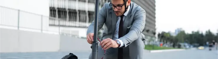 Un homme en costume et casque ajuste sa trottinette électrique dans un environnement urbain moderne.