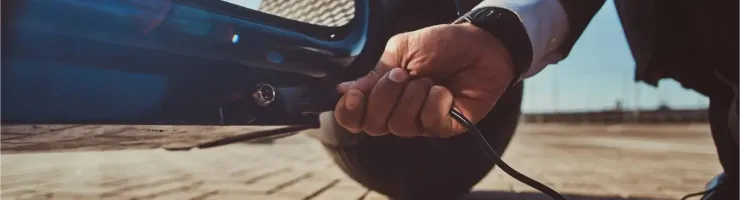 Gros plan sur une main branchant un câble de chargement à une trottinette électrique sur un sol pavé.