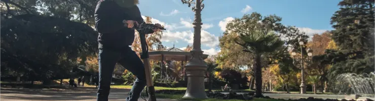 Un homme en casque et veste d'hiver se tient à côté d'une trottinette électrique dans un parc ensoleillé.