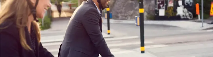 Deux personnes souriantes, casquées et en tenue de ville, font du vélo en milieu urbain.