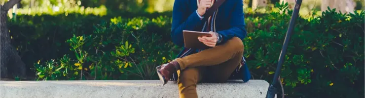 Un homme barbu assis sur un banc, pensif, avec sa trottinette électrique noire garée à côté de lui.