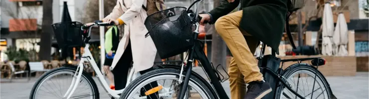 Un homme et une femme marchent à côté de leurs vélos de ville, avec des paniers à l'avant, en milieu urbain.