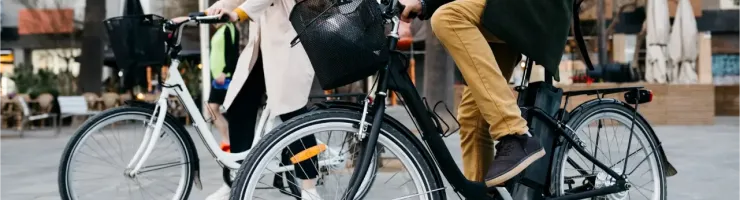 Un homme et une femme marchent à côté de leurs vélos de ville, avec des paniers à l'avant, en milieu urbain.