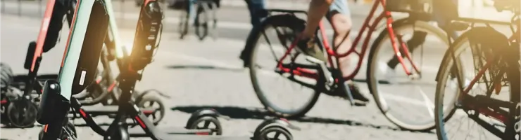 Plusieurs trottinettes électriques en libre-service sont garées sur un trottoir, avec des cyclistes en arrière-plan.