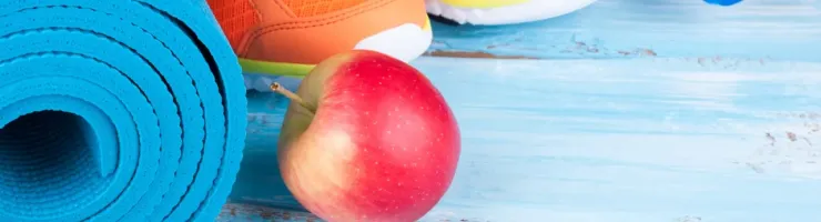 Équipement de sport : tapis de yoga, chaussures de running, bouteille d'eau et pomme.
