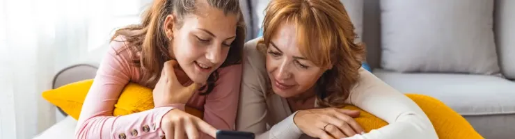 Mère et fille souriantes regardent un téléphone portable ensemble sur un canapé.