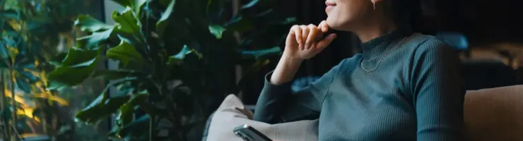 Femme pensive assise avec son téléphone, regardant par la fenêtre.