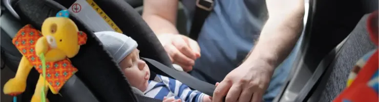 Un bébé attaché dans un siège auto, avec une personne ajustant les sangles.