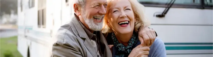 Un couple de personnes âgées souriantes et enlacées devant un camping-car, profitant de leur temps ensemble.
