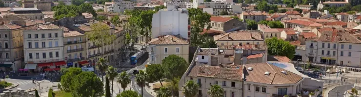 Vue panoramique de la ville de Nîmes (France) sous le soleil. Toits en tuiles, rues, arbres, tramway et ciel bleu.