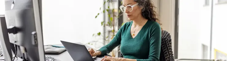 Une femme en chemise verte est assise à un bureau avec un ordinateur portable.