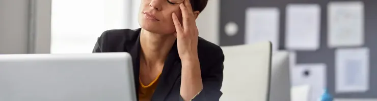 Une femme assise à un bureau, la tête dans les mains, semblant stressée ou préoccupée.