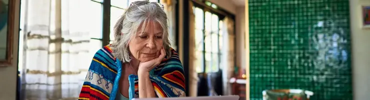 Une femme âgée assise à une table, utilisant un ordinateur portable.