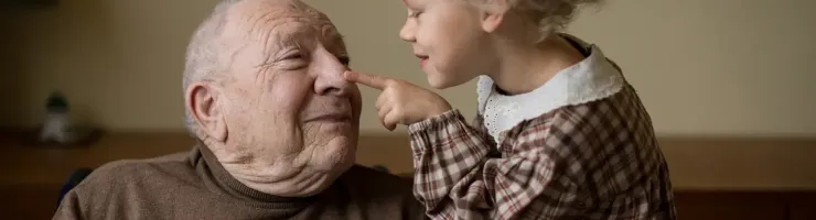 Une petite fille touche le nez de son grand-père avec un sourire, créant un moment tendre et joyeux entre eux.