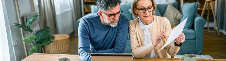 Couple senior examinant des documents sur un ordinateur portable, assis ensemble dans un environnement confortable.