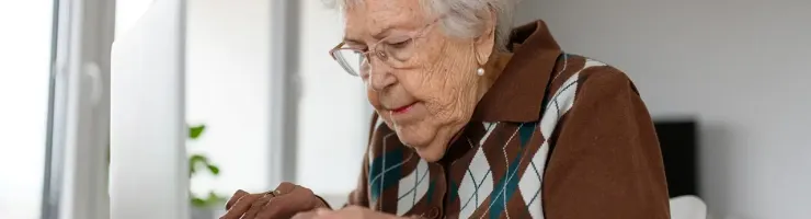 Une femme âgée utilise un ordinateur portable, concentrée sur l'écran.