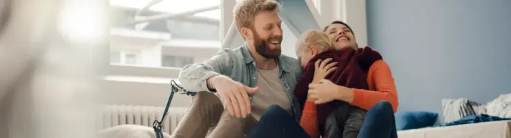Un père et une mère partagent un moment de complicité et de rires avec leur enfant dans leur maison.