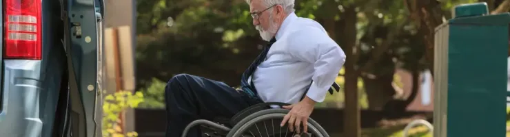 Un homme senior en fauteuil roulant utilise une rampe d'accès latérale pour descendre de son véhicule adapté.