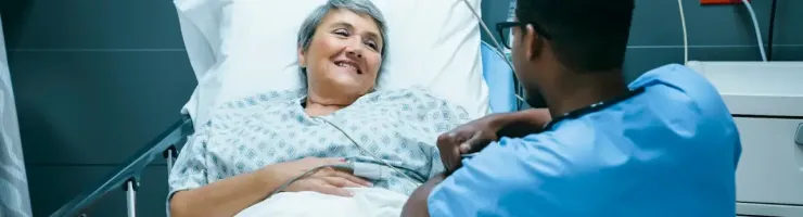 Une patiente souriante discute avec un infirmier dans une chambre d'hôpital équipée pour illustrer les soins.