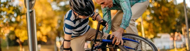 Un homme âgé aidant un enfant à se relever après une chute de vélo sur un chemin.