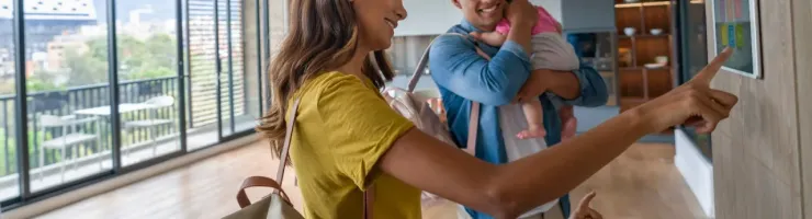 Famille souriante (parents et deux enfants) interagissant avec un panneau de contrôle mural de maison connectée.