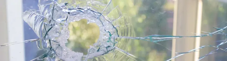 Gros plan sur une vitre brisée avec un impact central, fissurée, fond vert extérieur flou.