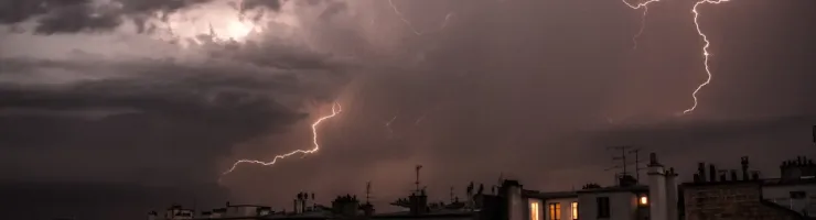 Orage violent au-dessus d'une ville la nuit, avec des éclairs zébrant le ciel sombre.