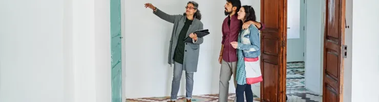 Une agente immobilière montre un détail d'une pièce vide à un couple dans un couloir avec un sol à motifs.