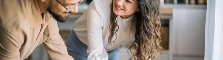 Un couple souriant signe des documents importants sur une table en bois, peut-être pour une propriété.