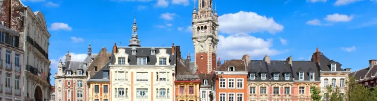 La Grand-Place de Lille : bâtiments colorés et beffroi sous un ciel bleu. Vie urbaine animée en terrasse.