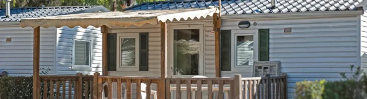 Un mobil-home de camping-car avec une terrasse en bois et un auvent, entouré d'arbres.