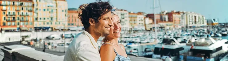 Couple heureux et souriant posant sur un balcon donnant sur un port de plaisance ensoleillé. 