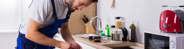 Un électricien ou réparateur utilise un multimètre pour tester une table de cuisson dans une cuisine.