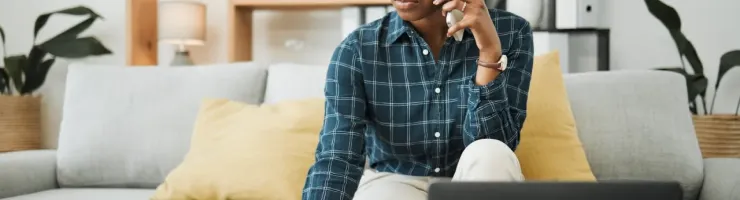 Femme d'affaires concentrée au téléphone, écrivant des notes sur un canapé confortable avec un ordinateur portable. Travail à domicile.