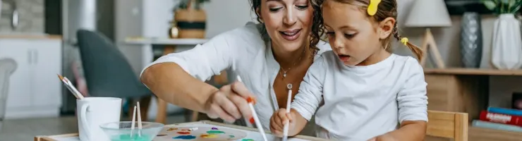 Une mère et sa jeune fille font de la peinture sur papier, assises à une petite table.