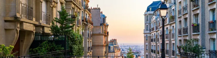 Ruelle pavée de Montmartre (Paris) avec rampes en fer forgé et lampadaire, bâtiments haussmanniens au coucher du soleil.