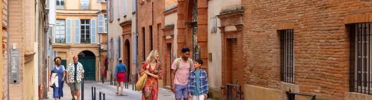 Une famille marchant dans une rue ancienne de Toulouse, bâtiments en briques rouges.