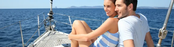 Un couple souriant assis sur le pont d'un voilier naviguant en pleine mer sous un ciel bleu.