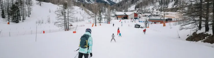 Vue de dos d'un skieur sur une piste de ski enneigée face à une station de montagne.