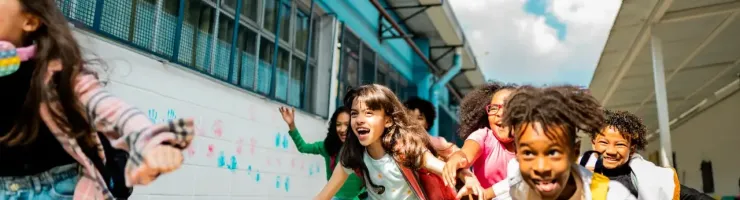Des écoliers dynamiques courent avec joie et énergie le long d'un mur blanc dans leur établissement scolaire.